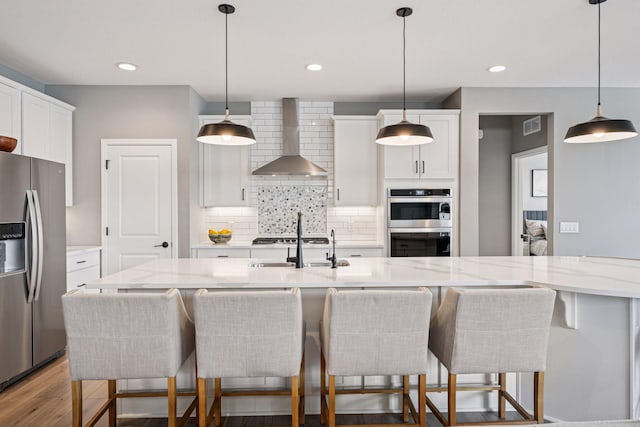 19477 102nd Pl, Corcoran, MN 55374 - kitchen featuring appliances with stainless steel finishes, wall chimney exhaust hood, backsplash, white cabinets, and a breakfast bar