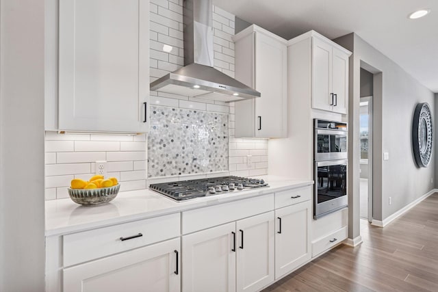 19477 102nd Pl, Corcoran, MN 55374 - kitchen featuring wall chimney range hood, appliances with stainless steel finishes, white cabinets, backsplash, and light wood-type flooring