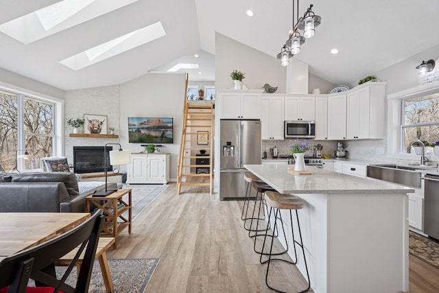 18837 Ogden St NW, Elk River, MN 55330 - kitchen featuring appliances with stainless steel finishes, a sink, a large fireplace, white cabinetry, and high vaulted ceiling