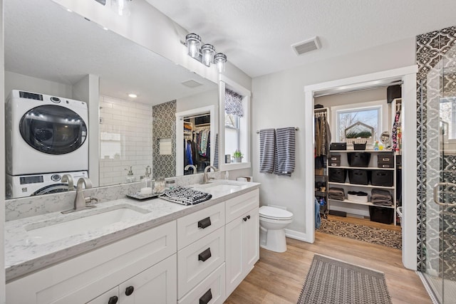 18837 Ogden St NW, Elk River, MN 55330 - full bathroom with stacked washer / dryer, double vanity, a walk in closet, toilet, and wood finished floors
