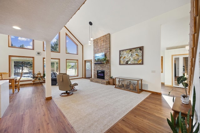 living room featuring wood finished floors, visible vents, baseboards, a fireplace, and high vaulted ceiling