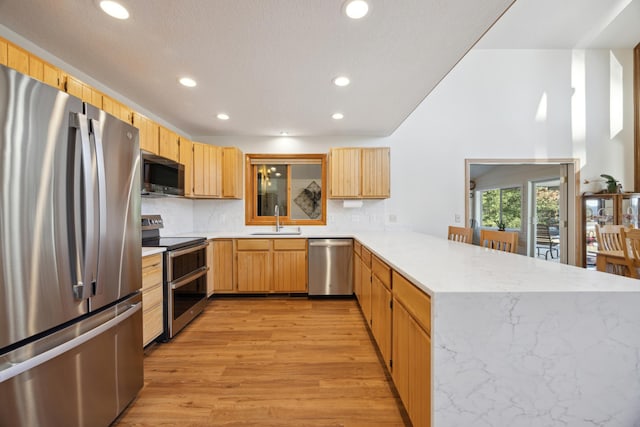 kitchen featuring recessed lighting, stainless steel appliances, a sink, a peninsula, and light wood-style flooring