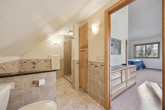 ensuite bathroom with tile walls, a textured ceiling, lofted ceiling, and a stall shower