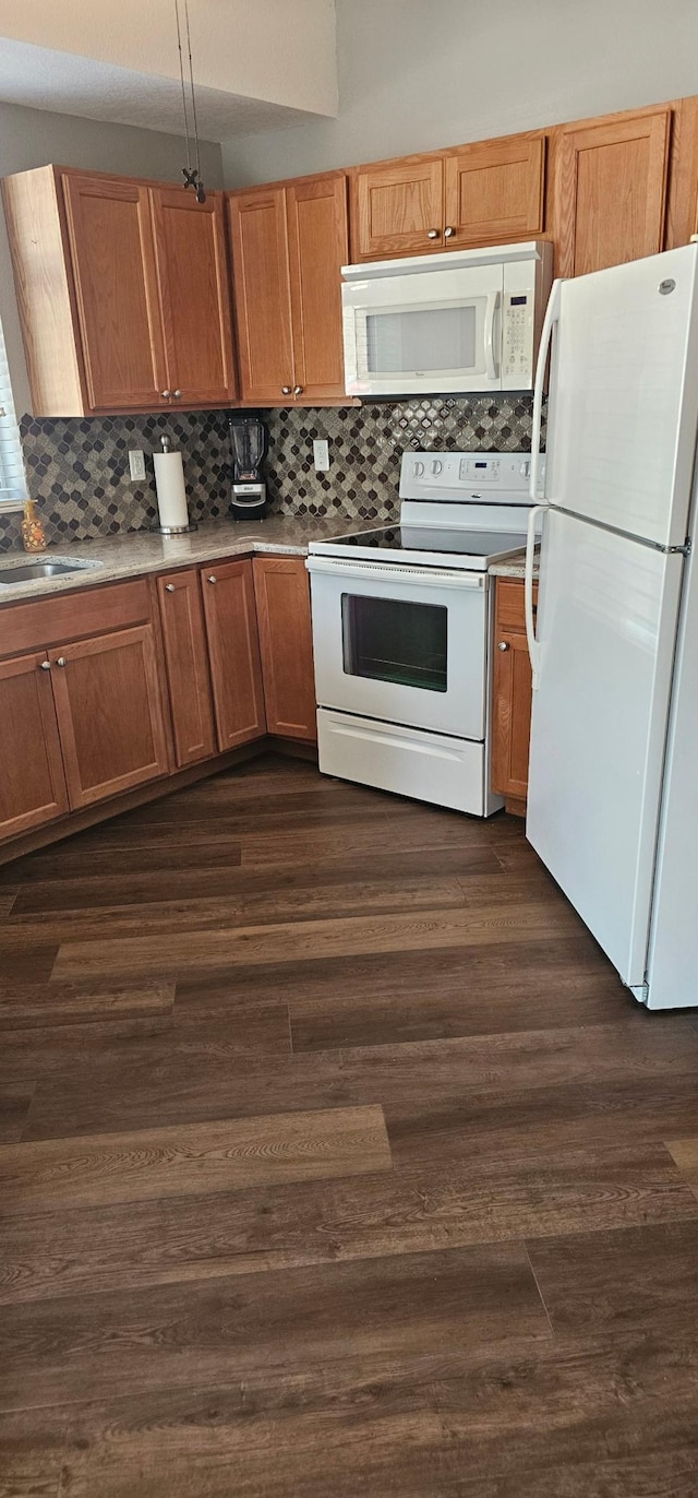kitchen with dark wood-style flooring, brown cabinets, white appliances, and backsplash