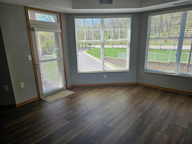 unfurnished room featuring baseboards, dark wood-style flooring, visible vents, and a textured wall