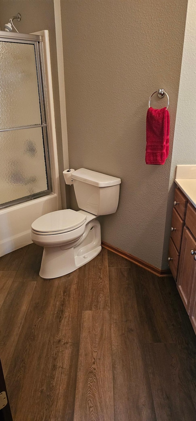 bathroom featuring toilet, bath / shower combo with glass door, baseboards, vanity, and wood finished floors
