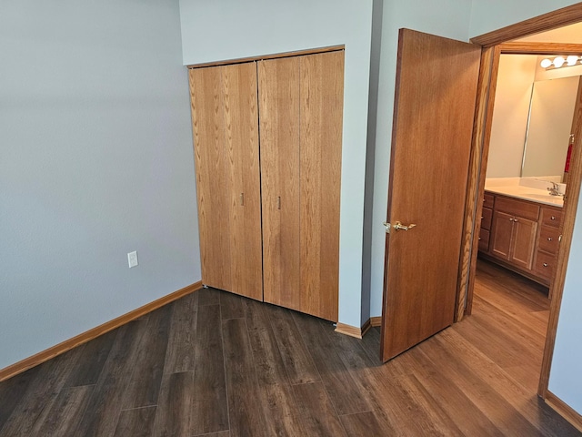 unfurnished bedroom featuring baseboards, dark wood-style flooring, a closet, and a sink