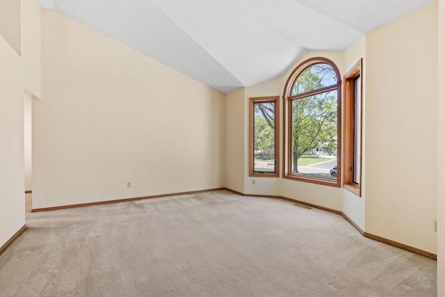 spare room with vaulted ceiling, light colored carpet, and baseboards