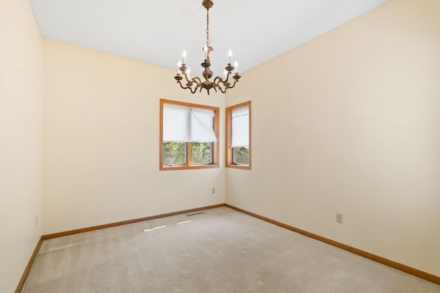empty room featuring a chandelier, baseboards, and light colored carpet