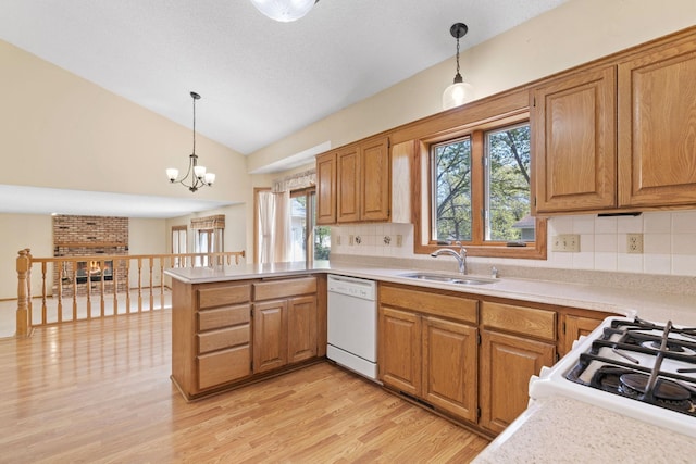kitchen featuring white dishwasher, a sink, a peninsula, vaulted ceiling, and light countertops