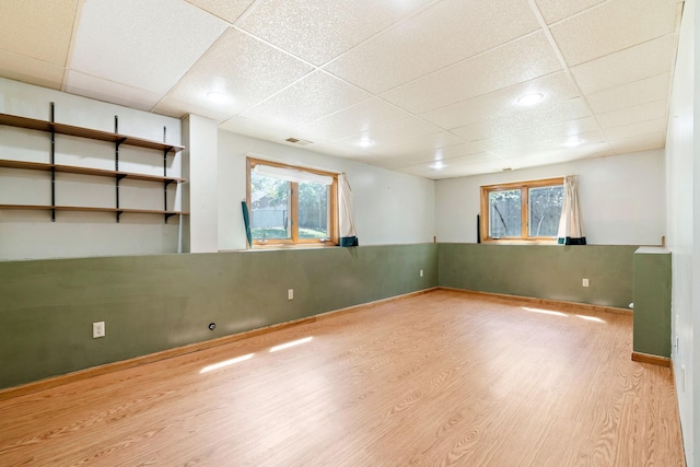 below grade area featuring a drop ceiling, wood finished floors, and plenty of natural light