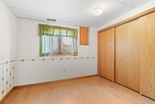 unfurnished bedroom with a drop ceiling, light wood-style flooring, a closet, and baseboards