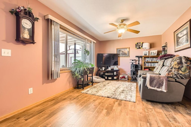 living area featuring a ceiling fan, baseboards, and wood finished floors