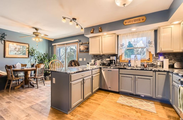 kitchen with stainless steel dishwasher, tasteful backsplash, a sink, and a peninsula