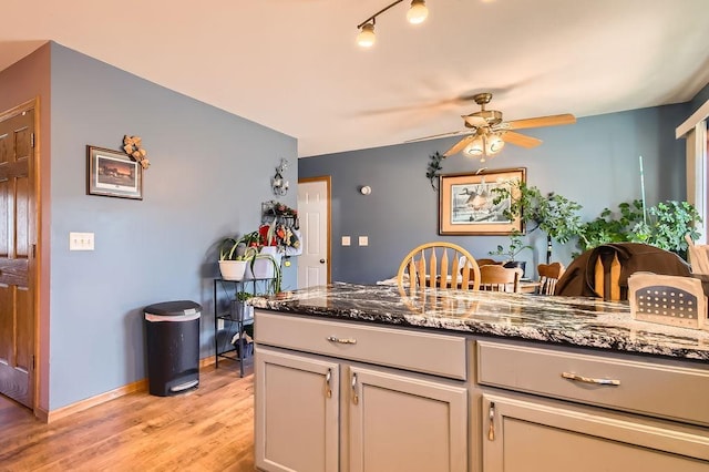 kitchen featuring dark stone counters, a ceiling fan, baseboards, and light wood-type flooring