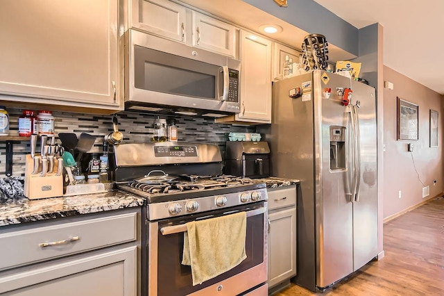 kitchen featuring light wood-style floors, stainless steel appliances, stone countertops, and decorative backsplash