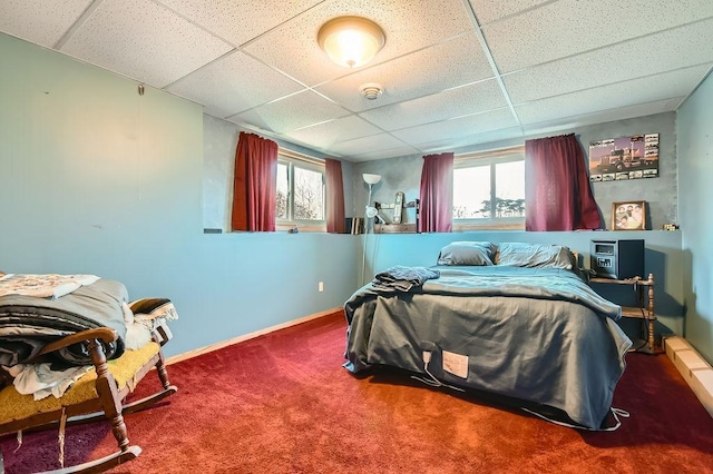carpeted bedroom with baseboards, a drop ceiling, and multiple windows