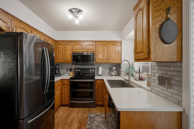 kitchen featuring a sink, tasteful backsplash, brown cabinets, black appliances, and light wood-style floors