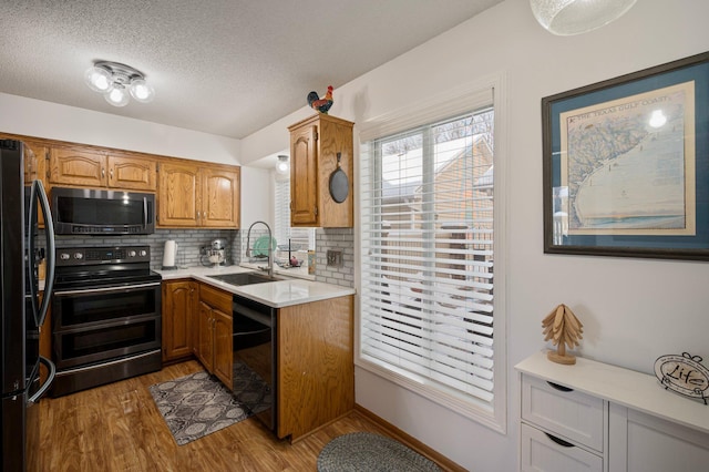 kitchen featuring light countertops, backsplash, a sink, light wood-style floors, and black appliances