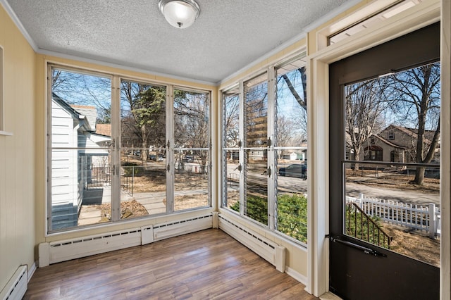 unfurnished sunroom featuring crown molding, a baseboard radiator, a textured ceiling, and wood finished floors