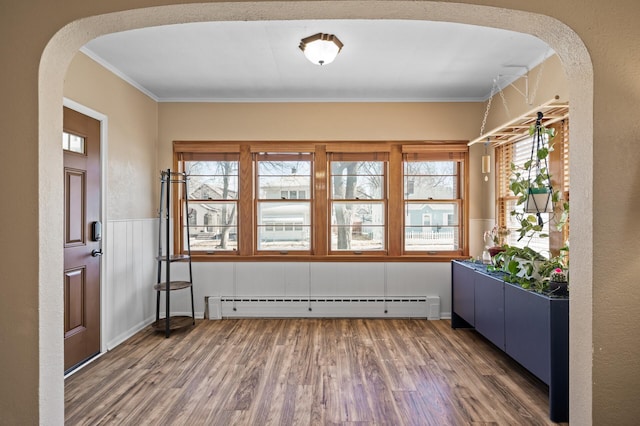 entrance foyer with crown molding, arched walkways, wainscoting, wood finished floors, and a baseboard heating unit