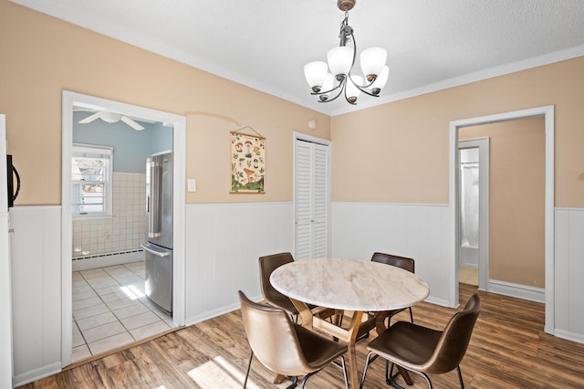 dining room with an inviting chandelier, wainscoting, a baseboard radiator, and light wood-style floors