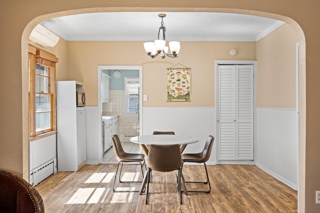 dining room with an inviting chandelier, wainscoting, baseboard heating, arched walkways, and light wood finished floors
