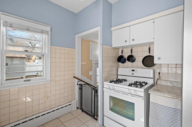 kitchen featuring light tile patterned flooring, tile walls, white range with gas cooktop, white cabinetry, and a baseboard radiator