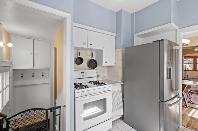 kitchen featuring decorative backsplash, white gas stove, stainless steel refrigerator with ice dispenser, light countertops, and white cabinetry