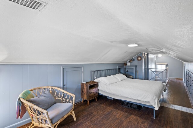 bedroom with a textured ceiling, visible vents, wood finished floors, baseboards, and lofted ceiling