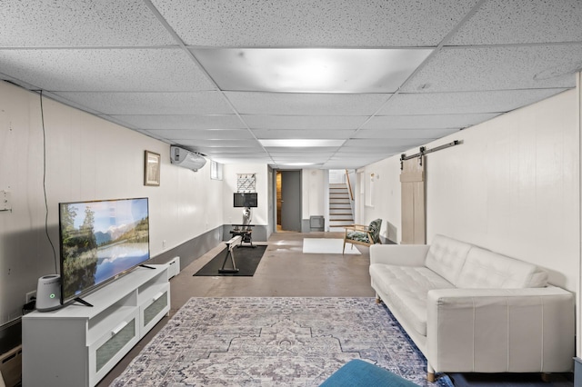 living room featuring an AC wall unit, a barn door, a paneled ceiling, and stairway