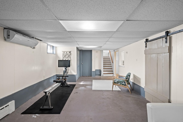 exercise area with a wall mounted AC, a barn door, baseboard heating, and a drop ceiling