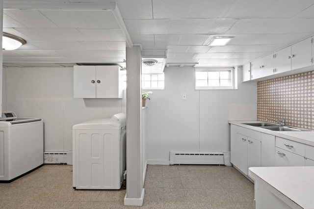 clothes washing area with visible vents, washing machine and clothes dryer, a sink, a baseboard radiator, and light floors