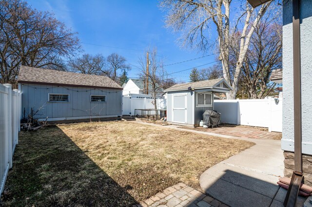 view of yard featuring a storage shed, an outbuilding, a fenced backyard, and a patio area