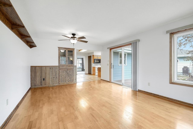 unfurnished living room with light wood-type flooring, a ceiling fan, and baseboards