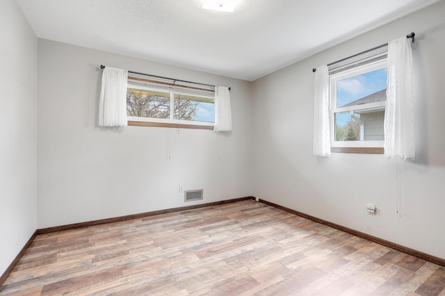 spare room with light wood-style floors, baseboards, and visible vents