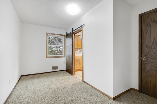 unfurnished bedroom featuring a barn door, visible vents, and light carpet