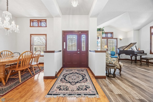entryway featuring vaulted ceiling, baseboards, a notable chandelier, and wood finished floors