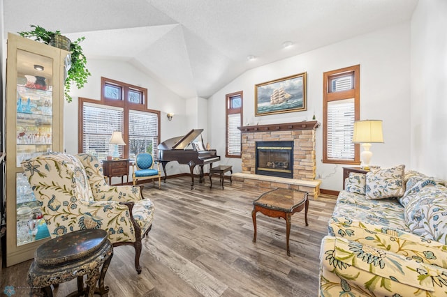 living area with baseboards, vaulted ceiling, wood finished floors, and a stone fireplace
