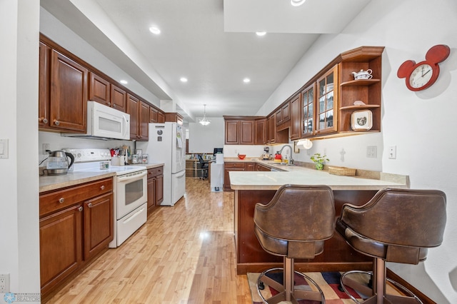 kitchen with a peninsula, a sink, light wood-style floors, white appliances, and light countertops