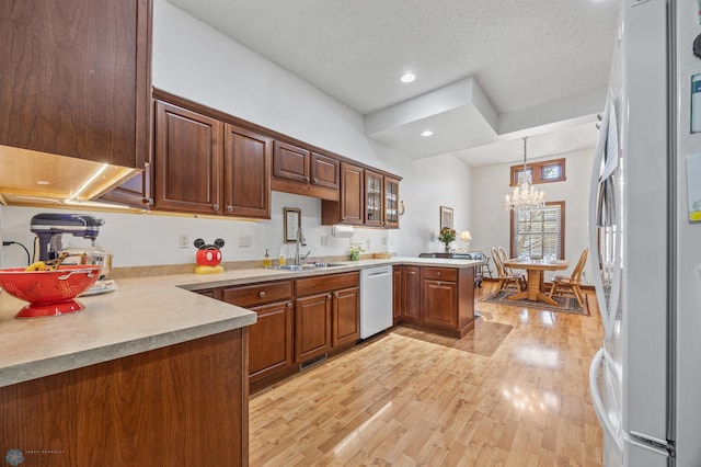 kitchen featuring a peninsula, light wood-style flooring, a sink, an inviting chandelier, and white appliances