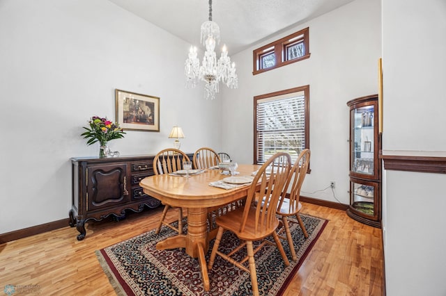 dining space with light wood-style floors, a towering ceiling, baseboards, and an inviting chandelier