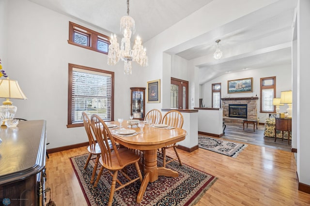 dining area featuring baseboards, a stone fireplace, a wealth of natural light, and a chandelier