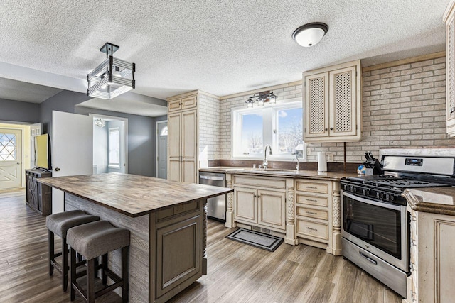 kitchen featuring a breakfast bar area, butcher block countertops, stainless steel appliances, a sink, and light wood finished floors