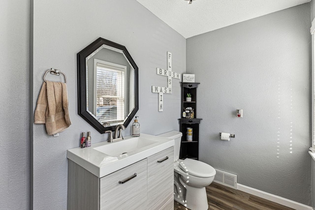 half bath with visible vents, baseboards, toilet, wood finished floors, and vanity