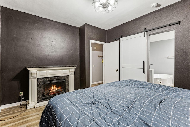 bedroom with a high end fireplace, light wood-style flooring, baseboards, and a barn door