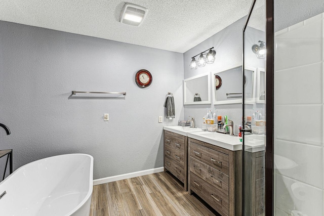 bathroom with a freestanding tub, wood finished floors, a textured ceiling, baseboards, and double vanity