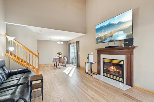 living room featuring stairway, wood finished floors, a high end fireplace, a towering ceiling, and an inviting chandelier