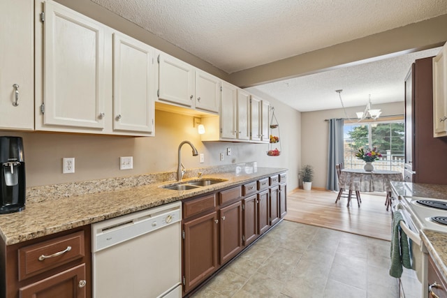 kitchen featuring a textured ceiling, white appliances, light stone countertops, a sink, and a notable chandelier