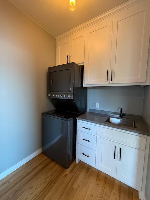 817 2nd St N, Brownsville, MN 55919 - kitchen featuring baseboards, stacked washing maching and dryer, white cabinetry, a sink, and light wood finished floors